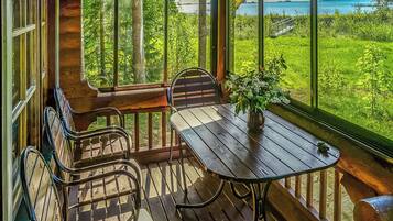 A wooden deck with a table and chairs, overlooking a lush green landscape and a body of water.