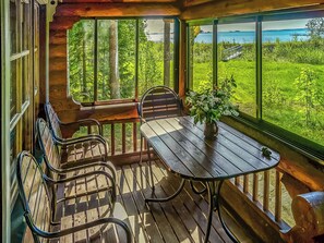 Eine Holzterrasse mit Tisch und Stühlen, mit Blick auf eine üppige grüne Landschaft und ein Gewässer.