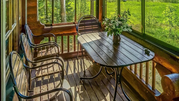 A wooden deck with a table and chairs, overlooking a lush green landscape and a body of water.