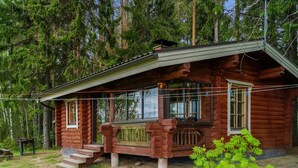 A rustic log cabin with a porch, surrounded by dense forest.