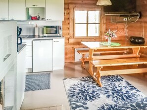 A compact kitchen with a refrigerator, microwave, and sink. There's a wooden dining table with benches and a vase of flowers. - Huvilakoti 2 by Interhome (Liperi)