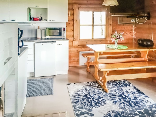 Eine kleine Küche mit Kühlschrank, Mikrowelle und Spüle. Ein Holztisch mit Bänken und eine Blumenvase.