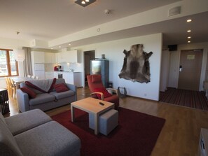 Ein stilvolles Wohnzimmer mit einer Couch, einem Sessel, einem Hocker, einem Flachbildfernseher und einem aufgehängten Tierfell.