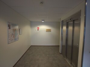 En gang med et kort på væggen, et nødudgangsskilt og en elevator.