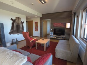 En moderne stue med et ophængt dyrehoved, en rød lænestol, en grå sofa, et sofabord og et fladskærms-TV.