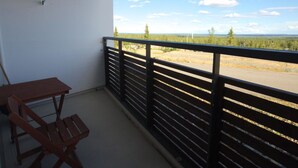 Un balcon avec une table et des chaises, une rambarde noire et une vue sur une route et des arbres.
