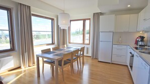 Une cuisine moderne avec des meubles blancs, une table à manger avec des chaises et de grandes fenêtres donnant sur l’extérieur.