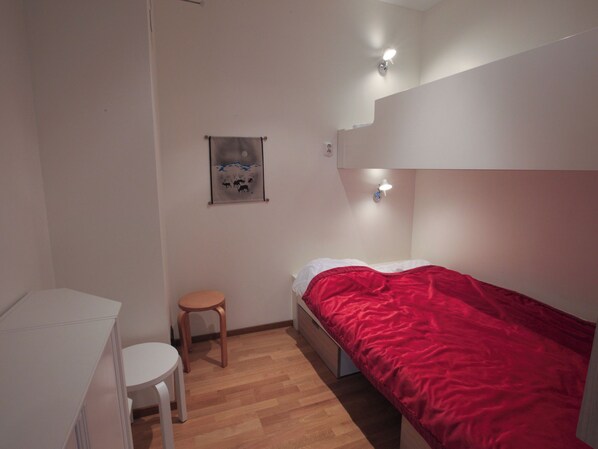 Et lille, pænt indrettet soveværelse med en enkeltseng, en stol, et skrivebord og en vægmonteret lampe.