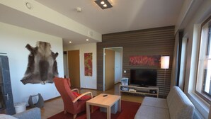 Un salon moderne avec un téléviseur à écran plat, un fauteuil rouge, un canapé gris et un tapis en fourrure.