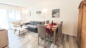 Ein modernes Wohnzimmer mit einer Couch, einem Esstisch und Stühlen. Ein Fenster mit Vorhängen, eine Stehlampe und Kunstwerke an der Wand sind ebenfalls vorhanden.