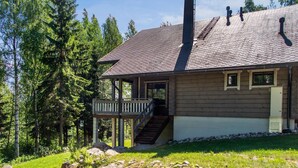 Une cabane dotée d’une véranda, d’une cheminée et offrant une vue sur la forêt environnante.