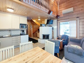 A compact kitchen with modern appliances, a dining area with a wooden table, and a cozy living space with a fireplace. - Kultakoto a by Interhome (Nilsiä)
