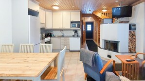 Une cuisine moderne avec des meubles blancs, un coin repas doté d’une table en bois et un salon avec un téléviseur et une cheminée.