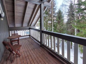 A wooden deck with a table and chairs, overlooking a snowy landscape with trees.