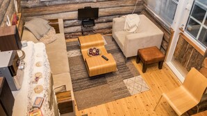 A cozy log cabin interior with a sofa, a coffee table, a television, and a fireplace.