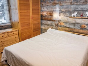 A bedroom with a wooden wardrobe, a bedside table, a lamp, and a wall with a rustic log design. - Ykkösruka 3, 3a by Interhome (Kuusamo)