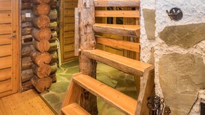 A wooden staircase leading to a log cabin interior with a stone wall and a wooden door.