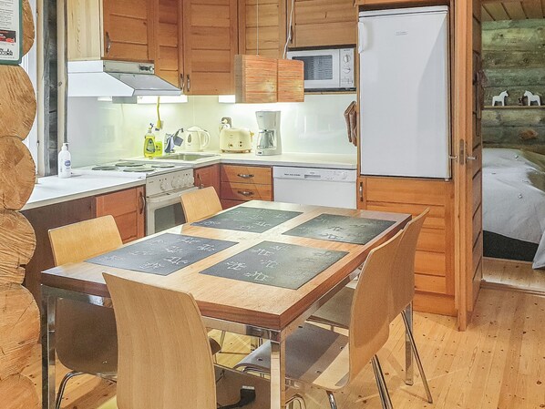 A compact kitchen with wooden cabinets, a stove, a refrigerator, and a dining table with chairs.