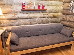 A log cabin interior with a wooden sofa, a small shelf with Christmas decorations, and a wooden floor.