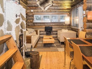 A log cabin interior with a stone wall, wooden furniture, a television, and a window with blinds. - Ykkösruka 3, 3a by Interhome (Kuusamo)