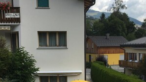 Il s’agit d’un bâtiment à deux étages doté d’un patio. On y trouve une table avec deux chaises et un parasol jaune. Une chaise blanche est également visible.