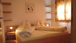 Une chambre confortable avec un lit en bois, une table de chevet avec une lampe, une étagère fixée au mur et une fenêtre avec des rideaux.