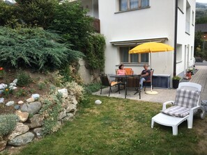Une terrasse extérieure avec une table et des chaises, un parasol jaune et une chaise blanche.