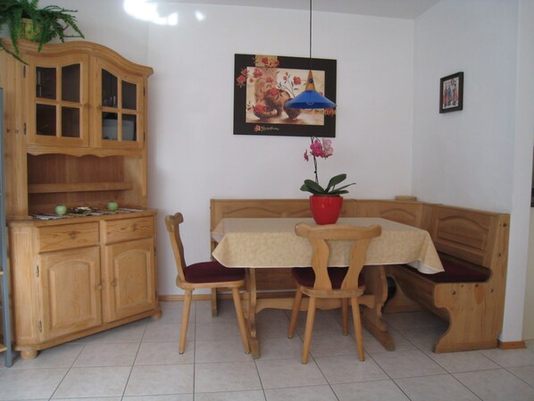 Un coin repas comprenant un buffet en bois, une table avec un pot rouge et des chaises.