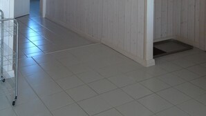 Ein Flur mit heller Holzvertäfelung, einem weißen Fliesenboden und drei gerahmten Bildern an der Wand.