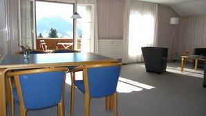 Ein Essbereich mit Tisch und Stühlen, Blick auf Berge durch große Fenster und einer Stehlampe.
