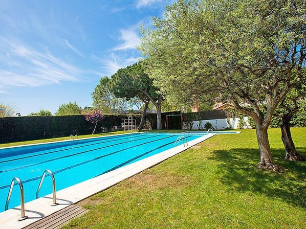A swimming pool with a wooden deck and metal handrails, surrounded by grass and trees. - Edificio Blanqueries by Interhome (Calella)