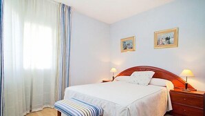 A neatly arranged bedroom with a bed, bedside tables, a bench, and two framed pictures on the wall. - Edificio Blanqueries by Interhome (Calella)