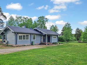 Een gelijkvloers huis met een veranda, schoorsteen en een gazon.