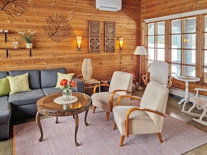 Ein gemütliches Blockhaus-Interieur mit einer Couch, Sesseln, einem Couchtisch und einer Lampe.