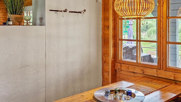 Un interior rústico de madera con un gran ventanal, una lámpara colgante y una mesa con un expositor de vidrio.