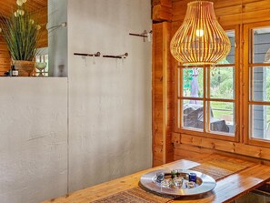 Un interior rústico de madera con un gran ventanal, una lámpara colgante y una mesa con un expositor de vidrio.