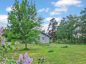 A house surrounded by a grassy yard with trees and purple flowers.