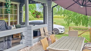 Un patio techado al aire libre con mesa y sillas, una parrilla, y un coche estacionado fuera.
