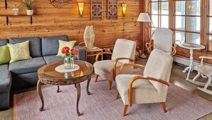 Interior acogedor de una cabaña de madera con un sofá, sillones, una mesita de centro y decoración en las paredes.