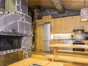 A rustic kitchen with a stone fireplace, wooden cabinets, and a wooden dining table.
