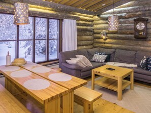 A cozy log cabin interior with a wooden dining table, a sofa, and a wall-mounted clock. - Rukakämmekkä by Interhome (Kuusamo)