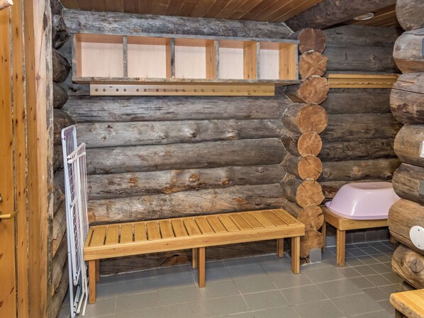 A log cabin interior with a wooden bench, a pink sink, and a metal rack.