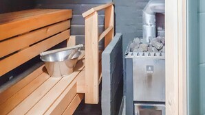 Un sauna avec des bancs en bois, un récipient en métal et un appareil de chauffage en pierre.