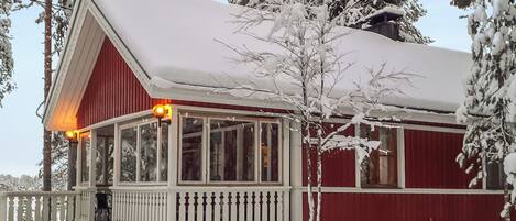 A snow-covered wooden house with a porch and a visible chimney.