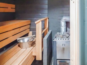 A sauna room with wooden benches, a metal basin, and a sauna heater. - Kaukosaaren ahonlaita by Interhome (Kuusamo)