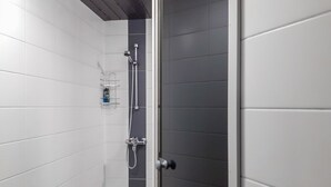 Une douche moderne avec une porte en verre, des murs recouverts de carreaux blancs et un élément décoratif vertical de couleur foncée.