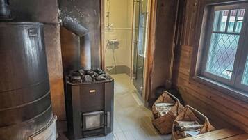 A rustic cabin interior with a wood-burning stove, a shower area, and a window with a view.