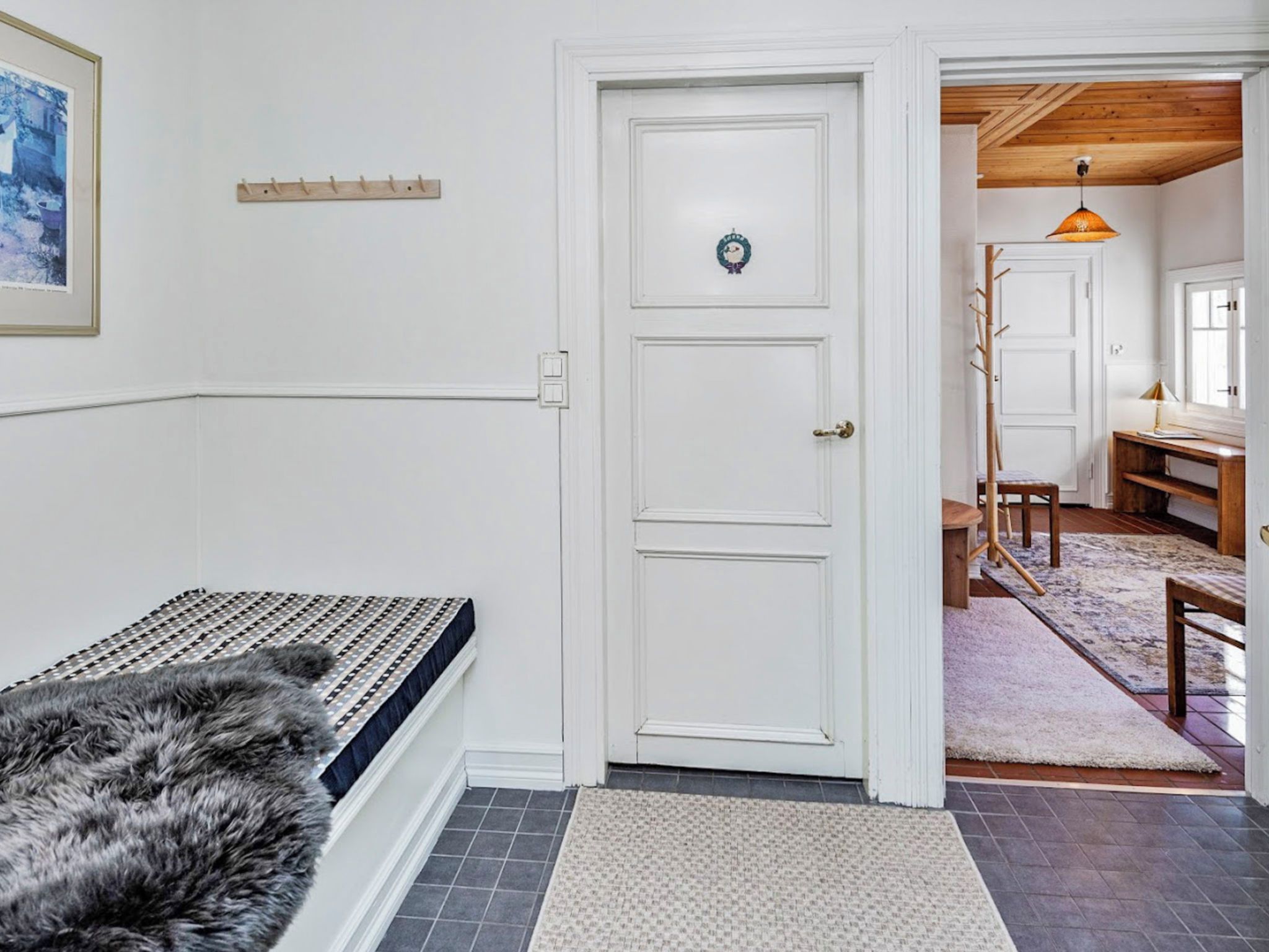 A room with a white door, a fur rug, a bench, and a wooden floor.