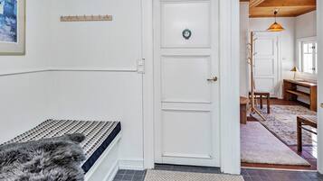A room with a white door, a fur rug, a bench, and a wooden floor.