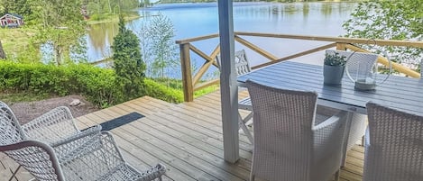 Een houten terras met buitenmeubilair, met uitzicht op een meer en een bebost gebied.